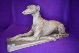 A resin cast figure of a resting grey hound signed PGG 1995 approx 50cm long