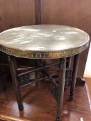 An eastern brass topped table with folding wooden carved base