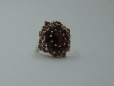 A garnet cluster dress ring in a claw set raised moulded mount on a 9ct gold loop, size M & 4.6g