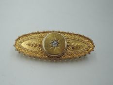 An oval yellow metal brooch stamped 15ct having a central diamond in a star burst mount within
