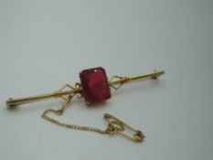 A yellow metal bar brooch stamped 9ct having a central red paste stone in a claw set box mount