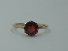 A small solitaire dress ring having a hessonite garnet style stone in a 6 claw setting on a rose