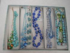 Nine strings of beads in shades of blue and green, some on yellow metal wire