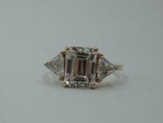 A synthetic clear three stone dress ring having a central emerald cut stone flanked by two