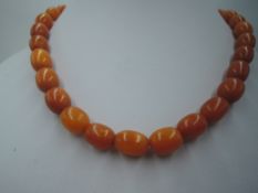 A short string of butterscotch amber beads of even oval form, with yellow metal clasp, approx
