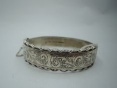 A silver hinged bangle having decorative edging and engraved scrolling. Approx 30.4g