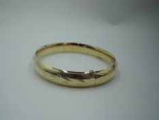 A yellow metal hinged bangle stamped 14K having slide clasp and engraved decoration, approx 13.5g