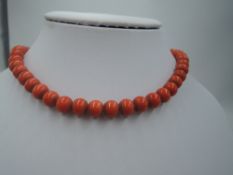 A string of carved coral beads of even form having a concealed coral and yellow metal clasp,