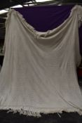 A vintage knitted bed cover having fringed edges.