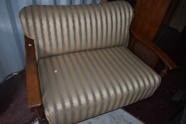 An early 20th Century oak and bergere frame settee having later gold and green stripe upholstery,