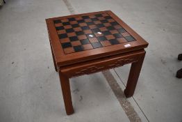 An Oriental hardwood games table, having chess board top and pieces to drawer