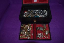 A vintage black jewellery case containing a selection of costume jewellery including brooches,