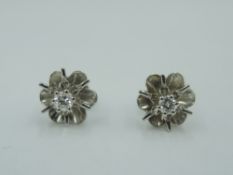 A pair of diamond stud earrings in white metal floral mounts