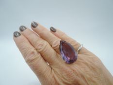 An over sized synthetic alexandrite pear shaped solitaire ring in a 4 claw set yellow metal basket