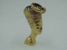 A yellow metal charm stamped 750 in the form of Egyptian Nefertiti bust with blue paste stone to
