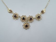 A 9ct gold necklace having five garnet set floral style panels to front, approx 16' & 5.3g