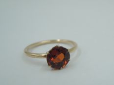 A small solitaire dress ring having a hessonite garnet style stone in a 6 claw setting on a rose