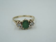 An emerald and diamond dress ring having a central oval emerald flanked by two diamonds to