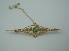 An Edwardian yellow metal bar brooch stamped 15ct having peridot and seed pearl decoration