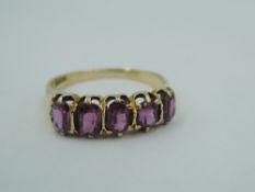 A yellow metal dress ring stamped 18ct having five oval purple/pink paste stones in a claw set