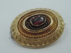 A oval yellow metal brooch having moulded decoration and central garnet to front and glass locket
