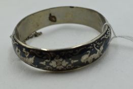 A white metal hinged bangle stamped Thailand/ Siamese having Niello enamelled Oriental decoration,