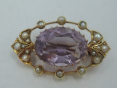 A small yellow metal oval brooch having a central amethyst in a claw set mount within an open seed