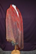 A Victorian paisley wool shawl having fringed edges,green, yellow and blue on red ground.
