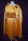 A 1950s gold satin two piece outfit comprising of dress with side pleats to skirt and round neckline