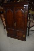 A Georgian oak corner cupboard having panelled doors and brass hinge, handle and escutcheons, key