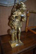 A gilt metal table lamp modelled as a piper in traditional dress, detail includes feather cap and