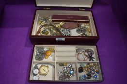 A wood effect jewellery case containing a selection of costume jewellery including clip earrings,