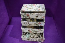 A four drawer retro cardboard chest containing a selection of costume jewellery and strings of beads