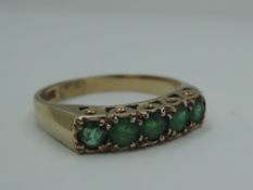 A five stone emerald ring in a gallery mount on a 9ct gold loop, size Q and approx 2.8g