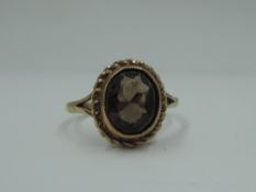 A smoky quartz solitaire dress ring in a collared mount with rope wire decoration on a 9ct gold