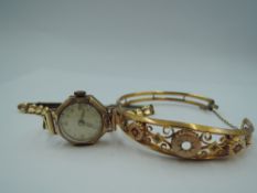 A 9ct gold hinged bangle having decorative panel with red paste and diamond chips, central stone