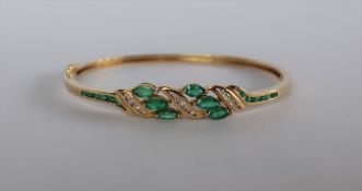 A 14ct yellow gold emerald and diamond set hinged bangle,
