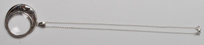 A SILVER PENDANT MAGNIFYING GLASS IN THE FORM OF A CRESCENT MOON