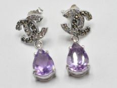 A pair of silver crossed C earrings set with pear cut amethyst drops, with marcasite's and white
