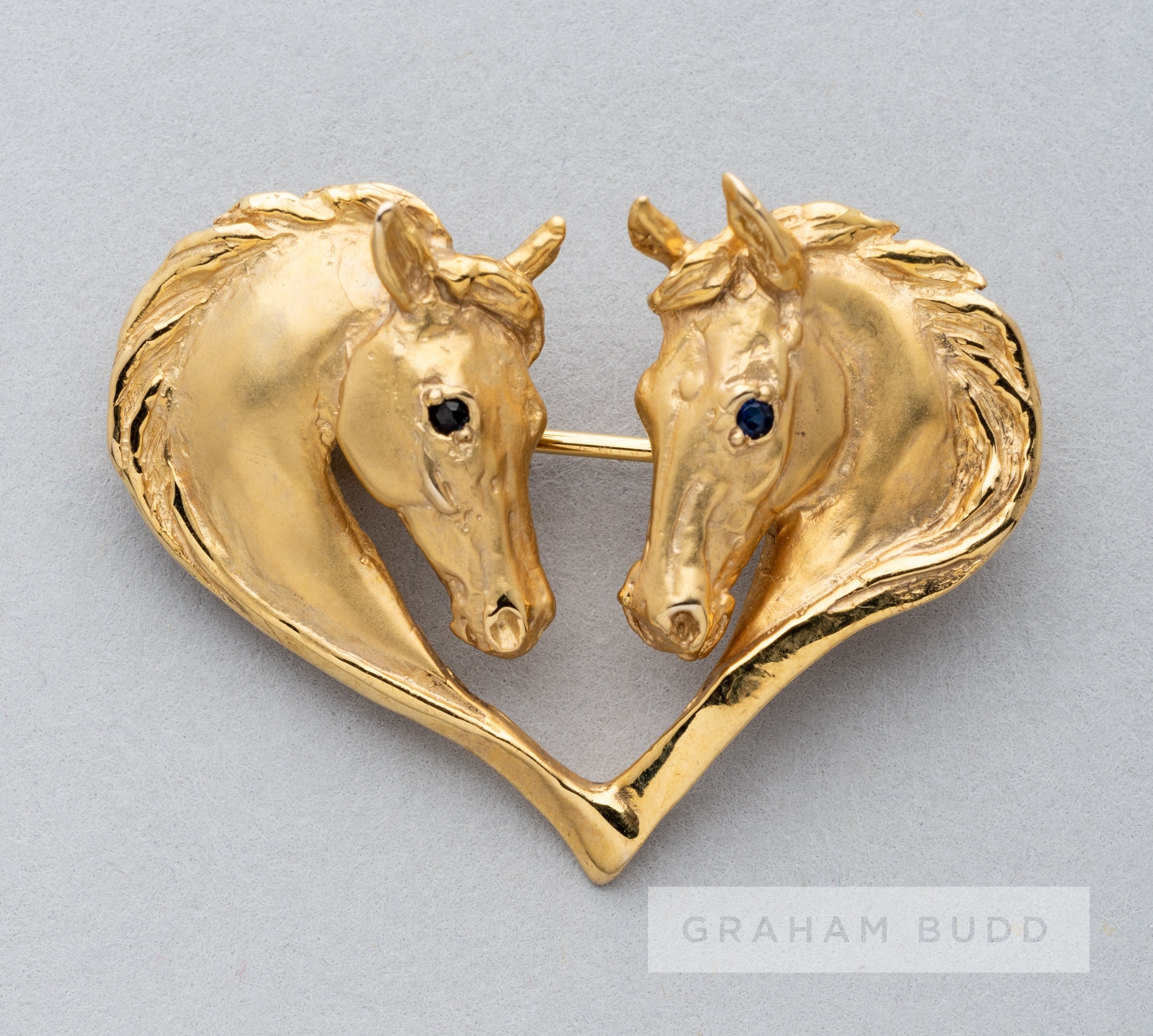 A Harriet Glen 9ct gold and blue sapphire horsehead heart brooch, modelled as two horse heads with