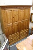 A modern pine wardrobe with two large doors above four drawers.
