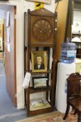 An Arts and Crafts oak long case clock, the face with brass numerals and hands, above open shelves.
