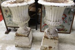A pair of painted cast iron garden urns on pedestal bases.