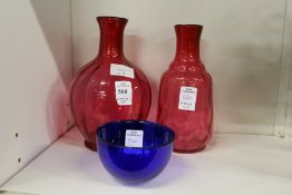 Two cranberry glass bottle vases and a blue glass bowl.