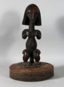 A CARVED TRIBAL AFRICAN FIGURE on an oval base. 19ins high.