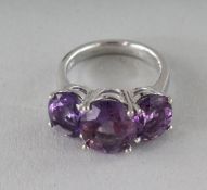 A SILVER THREE-STONE OVAL CUT AMETHYST RING.