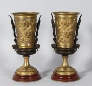 A PAIR OF CLASSIC BRONZE AND GILT BRONZE URNS on circular bases. 9.5ins high.