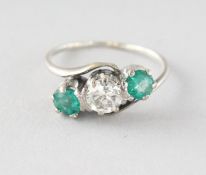 AN 18CT GOLD THREE-STONE DIAMOND AND EMERALD RING.
