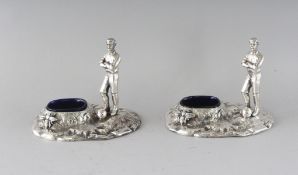 A PAIR OF PLATED FOOTBALLER SALTS with blue glass liners.