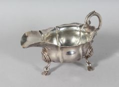 A GEORGE II CAST SILVER SAUCEBOAT, waved edge, crest, on three pad feet. London 1743.